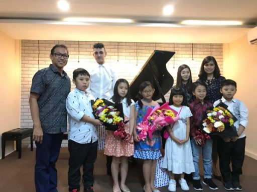 Gruppe von Kindern und Erwachsenen mit Blumensträußen vor einem Klavier.