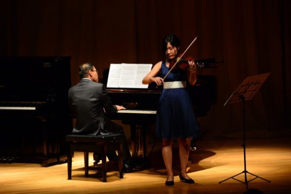 Eine Violinistin spielt auf der Bühne, begleitet von einem Pianisten.
